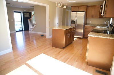 Open kitchen with wooden floors, island, and stainless steel appliances, next to entryway.