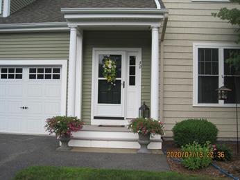 Green and cream house entrance with white door, flower pots, and a garage on the left.