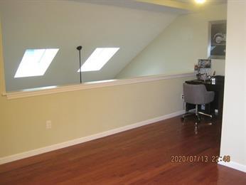 Loft area with wood floor, skylights, and a small desk with a gray chair in the corner.