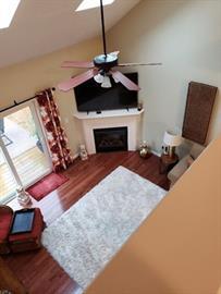 Living room with fireplace, TV, ceiling fan, white rug, and sliding glass door.