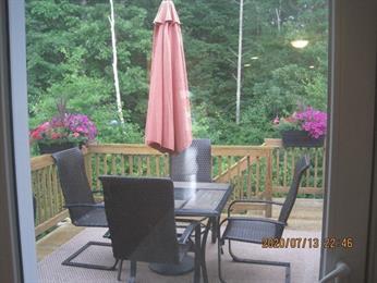 Patio table with four chairs and an umbrella, surrounded by flowers and trees outside.