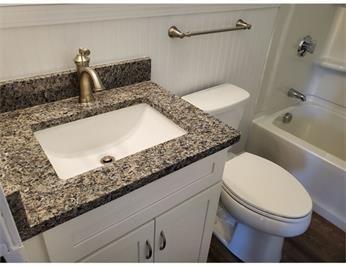 Bathroom with a granite countertop sink, white toilet, and bathtub with shower.