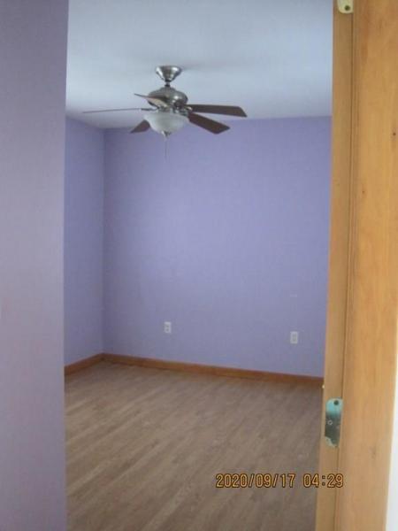 Empty room with purple walls, wood floor, and ceiling fan, viewed from an open door.