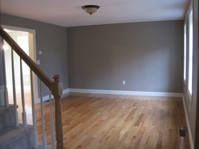 Empty room with hardwood floors, gray walls, and a staircase with beige carpet.