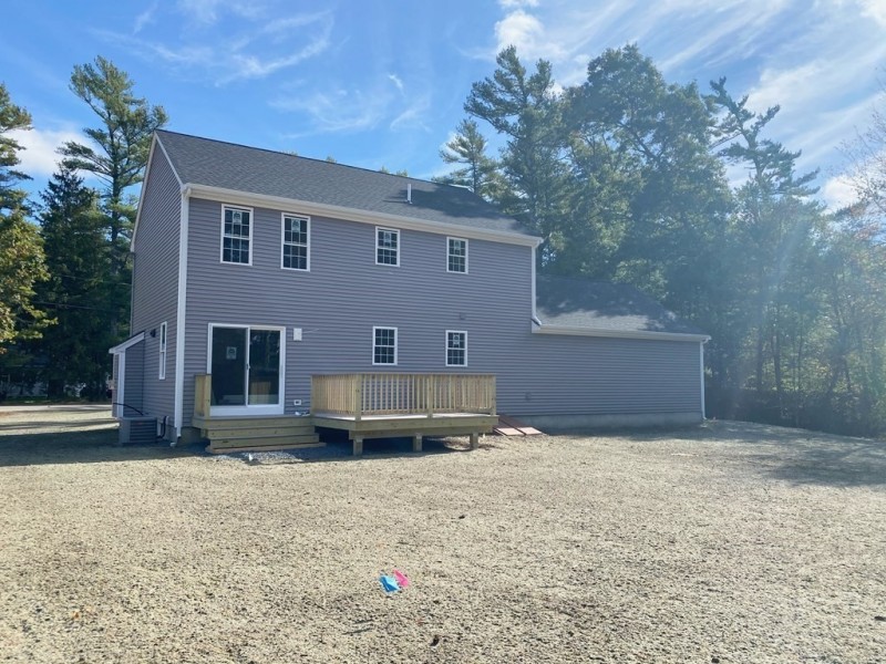 Two-story gray house with a small wooden deck and gravel yard, surrounded by trees.
