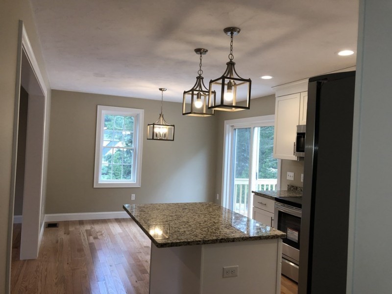 Modern kitchen with granite island, pendant lights, wood floors, and large windows.