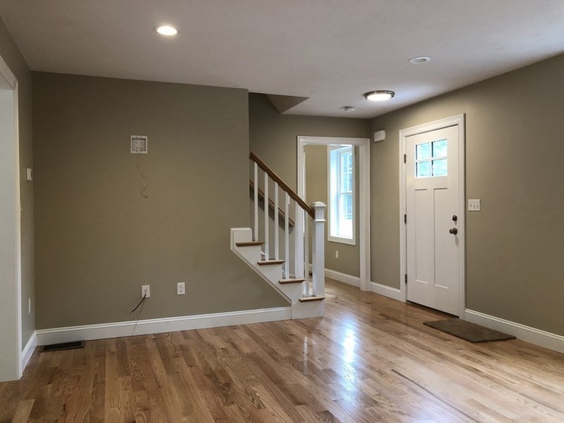 Empty room with wood floor, beige walls, white trim, stairs, and a white front door.