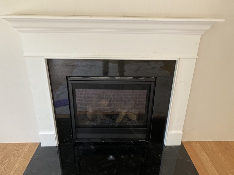 A white mantel fireplace with a black tile surround and wooden floor.