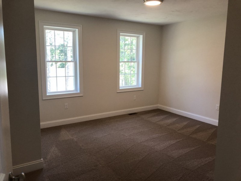 Empty room with light brown carpet, two windows, and light-colored walls.