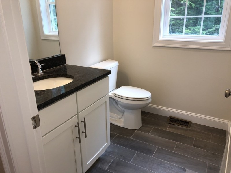 Modern bathroom with white cabinets, black countertop, toilet, and large window.