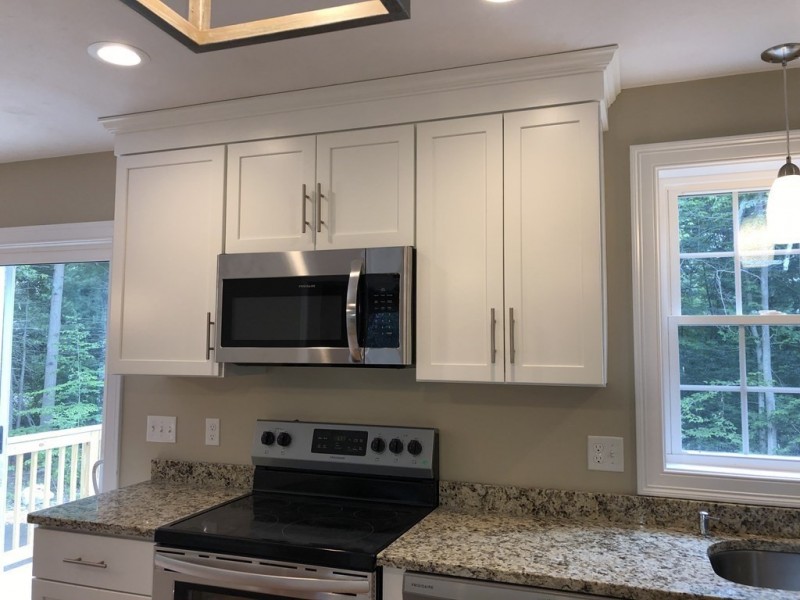 White kitchen cabinets over a microwave and stove, with granite countertops and windows.