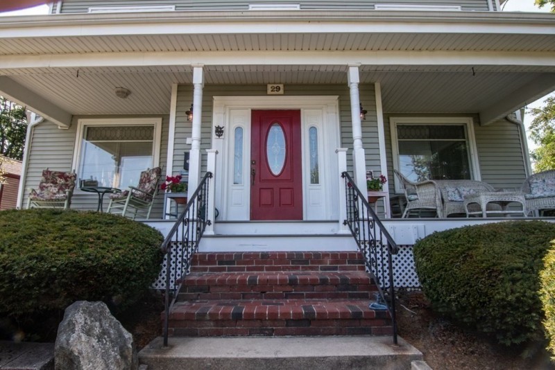 Front porch of a house with a red door, white columns, and outdoor seating on both sides.