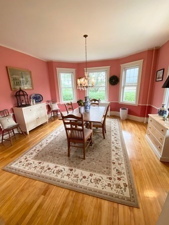 Dining room with pink walls, a chandelier, wooden table, and large windows.