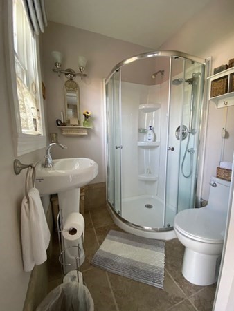 Small bathroom with a pedestal sink, glass shower, toilet, and striped rug on the floor.