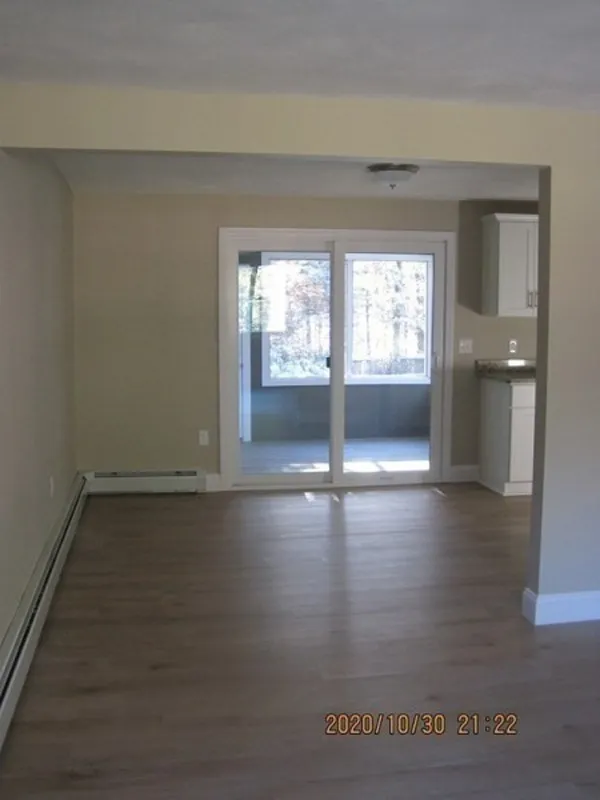 Unfurnished room with wood floors, beige walls, and sliding glass doors to a sunroom.