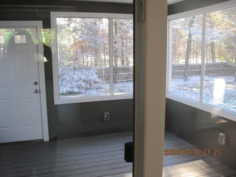 Enclosed porch with large windows showing a snowy yard and trees outside.