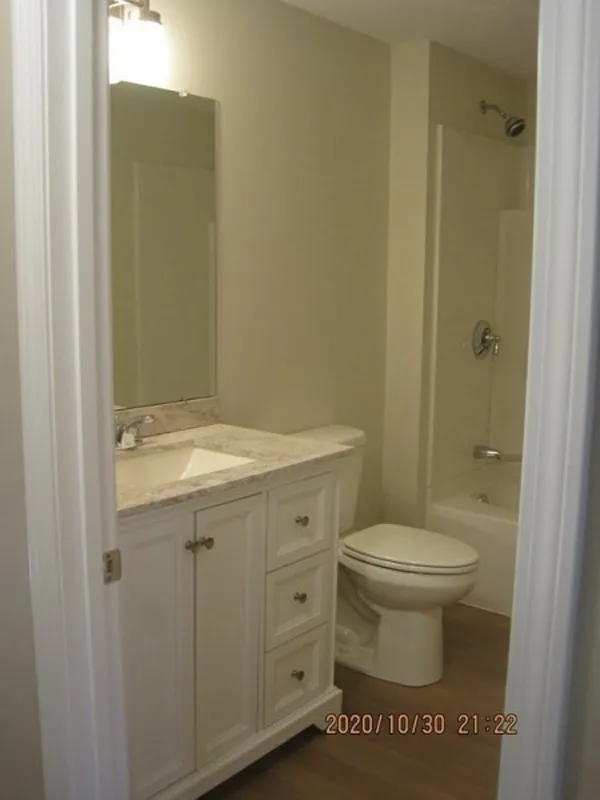Small bathroom with a white vanity, toilet, and bathtub-shower combo, beige walls.