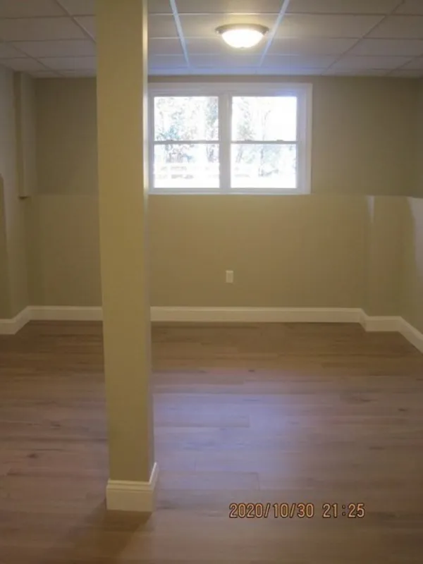 Empty room with wood floors, beige walls, a support column, and a window letting in light.
