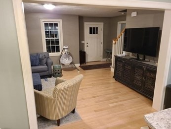 Living room with a sofa, armchair, baby swing, TV, and front door visible.