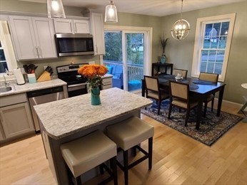 Modern kitchen and dining area with island, flowers, and large windows overlooking a yard.