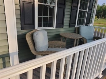 Two wicker chairs with cushions and a small table on a porch with green siding.