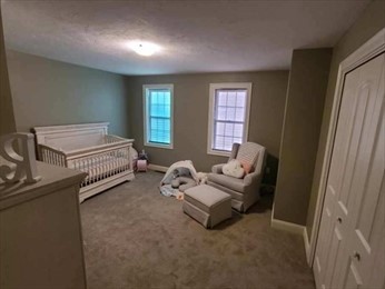Neutral-toned nursery with crib, rocking chair, ottoman, and soft toys on carpeted floor.