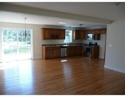 Spacious kitchen with wooden cabinets, hardwood floors, and sunlight from glass doors.