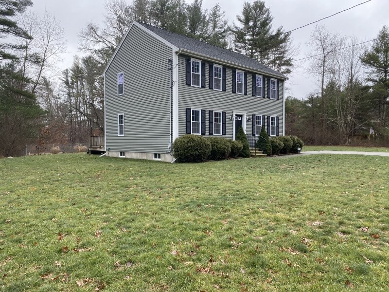 A two-story gray house with black shutters and a large grassy yard.