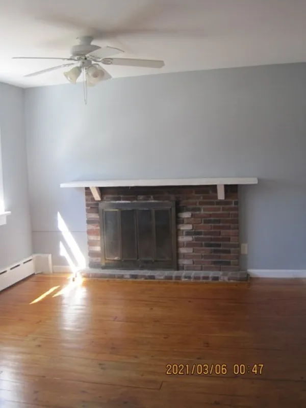 Living room with a brick fireplace, wood floor, gray walls, and a ceiling fan.