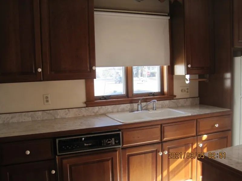 Kitchen with brown cabinets, marble countertop, sink, window, and dishwasher below.