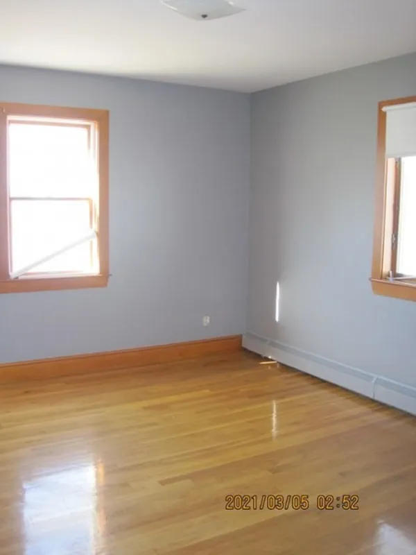 Empty room with light gray walls, wood trim, hardwood floors, and two windows.