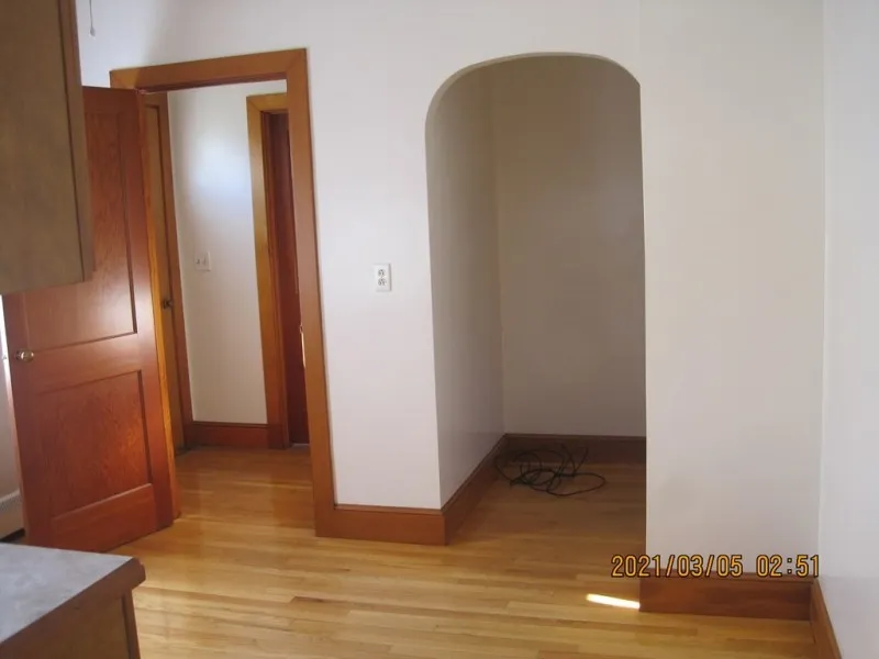 Small empty nook with wood trim and hardwood floor next to an open door in a bright room.