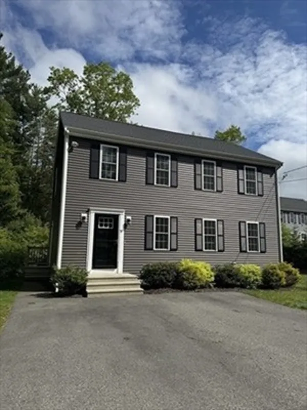 Two-story gray house with black shutters, front steps, and a driveway under a partly cloudy sky.