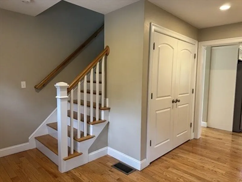 Small wooden staircase next to double-door closet in a hallway with hardwood floors.