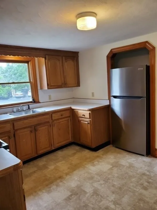 Kitchen with wooden cabinets, a stainless steel fridge, and a window above the sink.