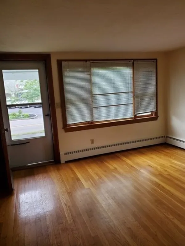 Empty room with hardwood floors, a window with blinds, and a door to the outside.