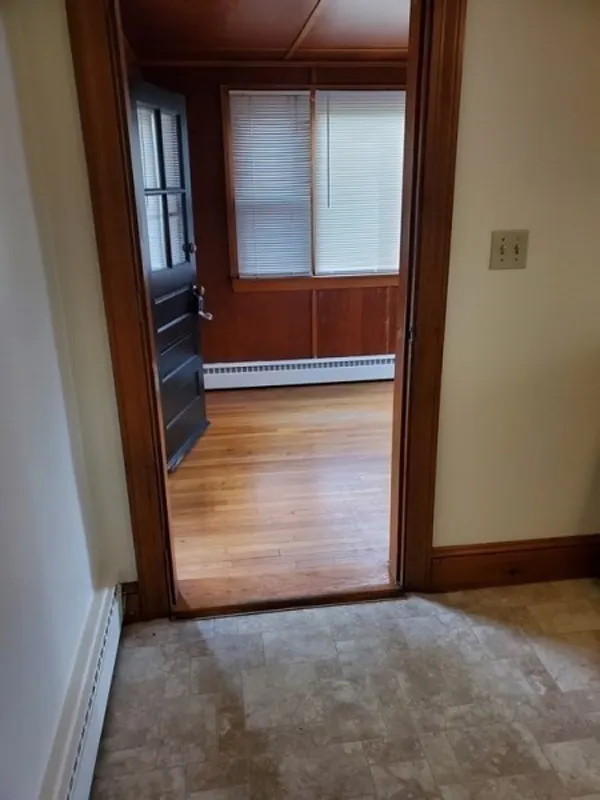 A doorway leads from a tiled floor to a room with wooden floors and closed blinds.