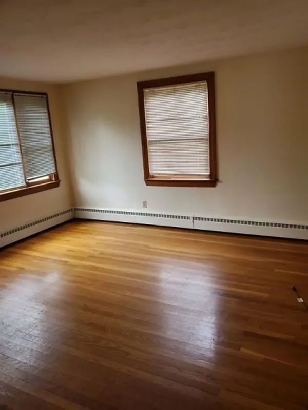 Empty room with hardwood floor, cream walls, and two windows with closed blinds.
