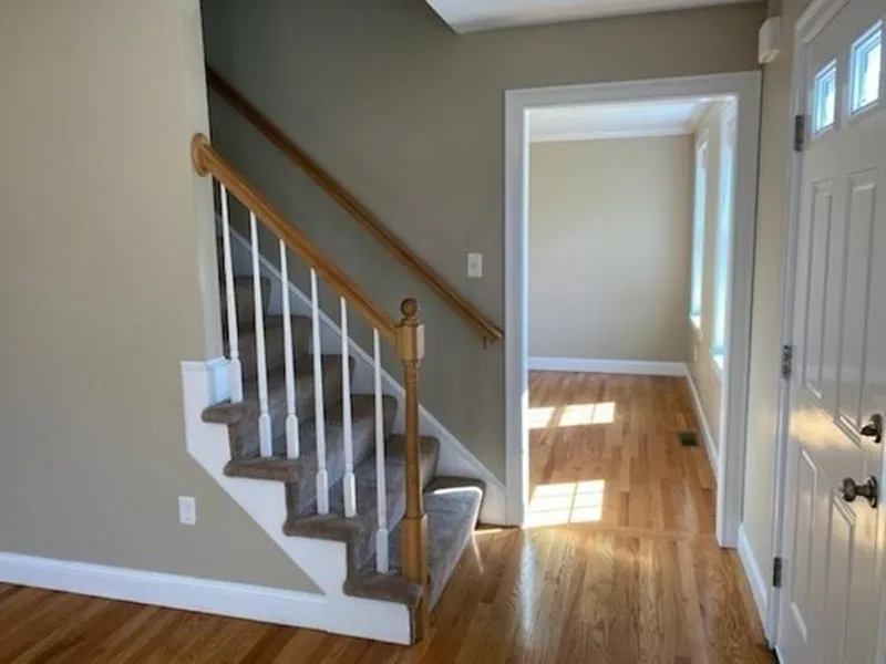 Carpeted staircase next to a white door, leading to a sunlit room with hardwood floors.