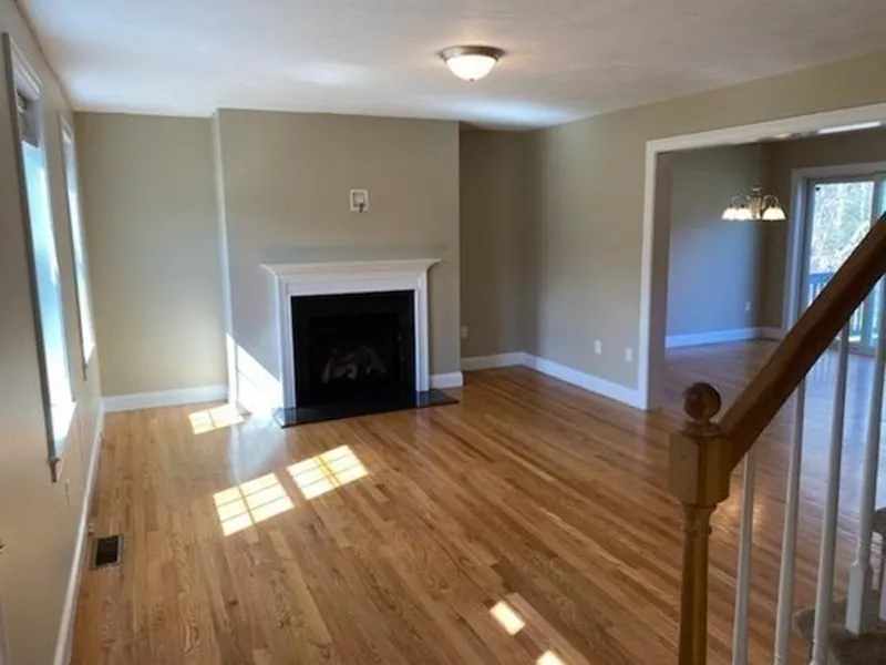 Empty living room with hardwood floors, a fireplace, and a staircase at the right.
