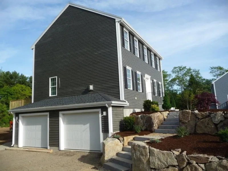 Two-car garage beneath a dark gray, two-story house with stone steps and landscaping.