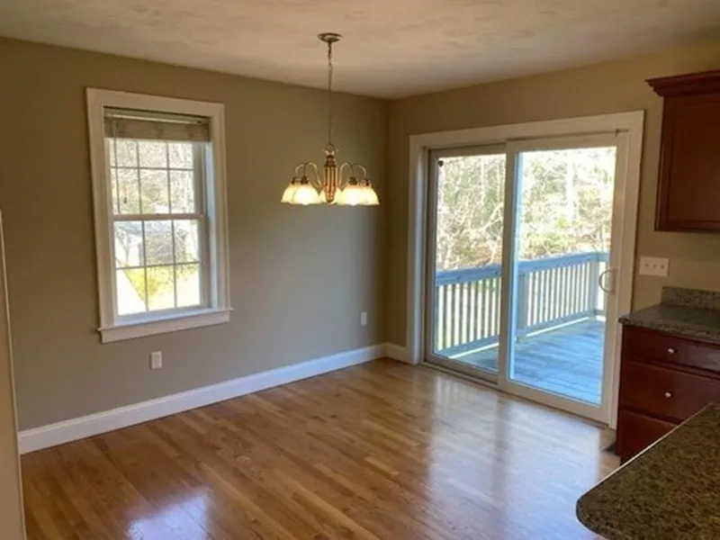 Bright dining area with wooden floor, window, chandelier, and sliding glass doors to a deck.