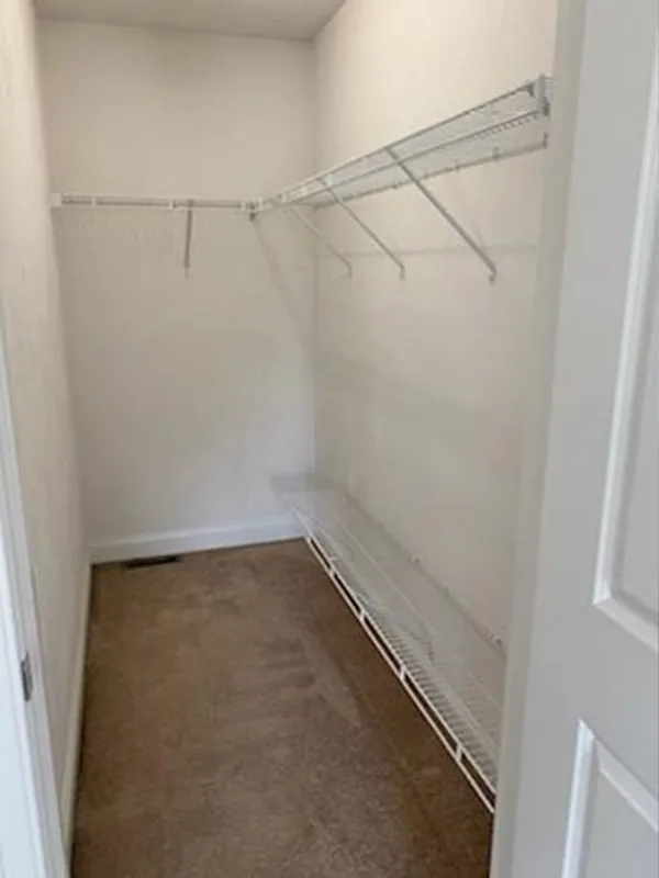 Empty walk-in closet with white wire shelves on the right wall and beige carpeted floor.