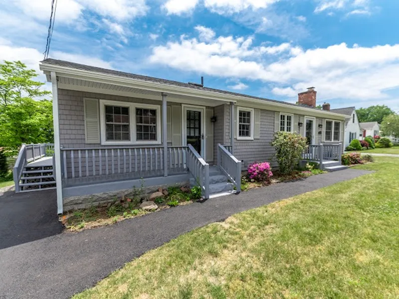 Gray ranch-style house with a porch, front steps, and flowers, on a sunny day.