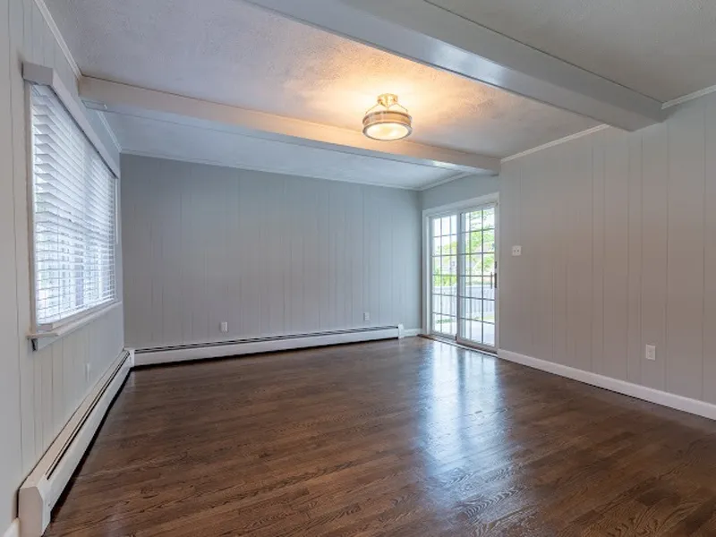 Empty room with hardwood floors, gray walls, ceiling light, and large windowed door.