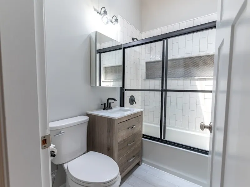 Modern bathroom with a wood vanity, white toilet, and shower with black-framed glass doors.