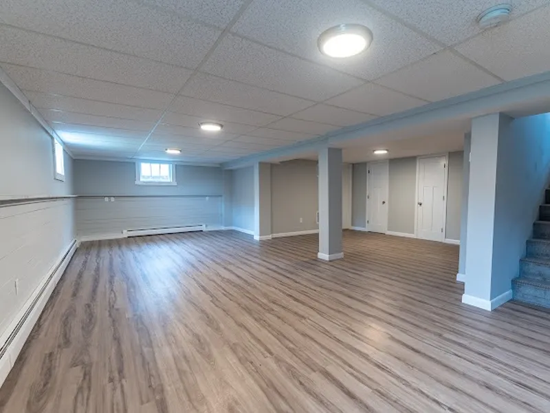 Spacious, empty basement with wood flooring, gray walls, and a staircase on the right.
