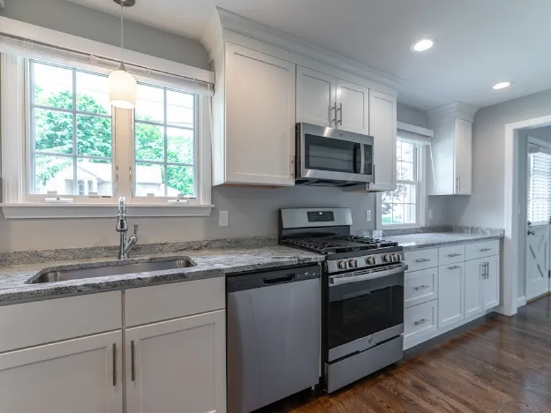 Modern kitchen with white cabinets, stainless steel appliances, and a large window.