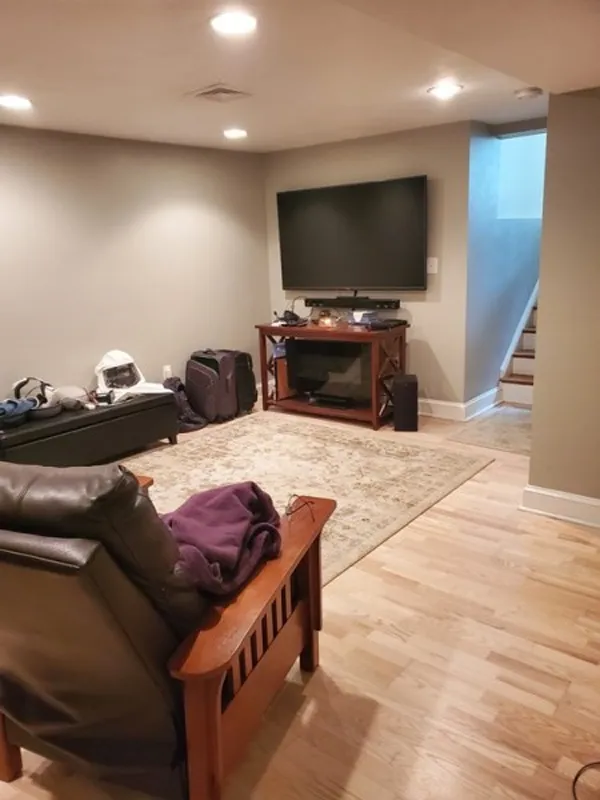 Basement living room with a TV, armchair, rug, and stairs leading up.