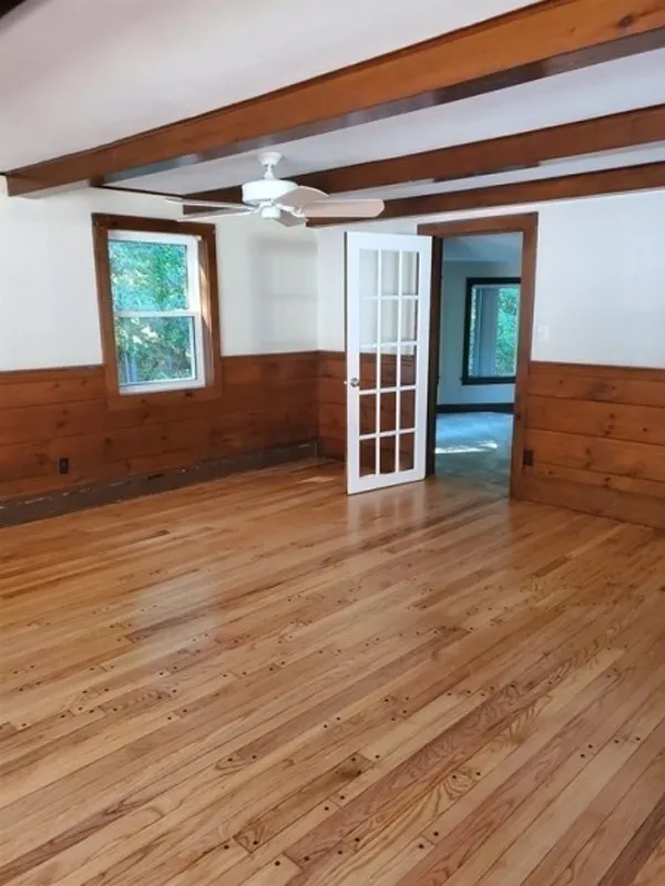 Empty room with wood floors, wood paneling, ceiling beams, and a glass-paneled door.